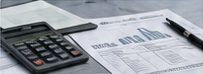 Desk scene of a calculator lying on printed financial documents and charts.