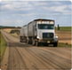 Related-story thumbnail showing a truck on a rural dirt road beneath a cloudy prairie sky.